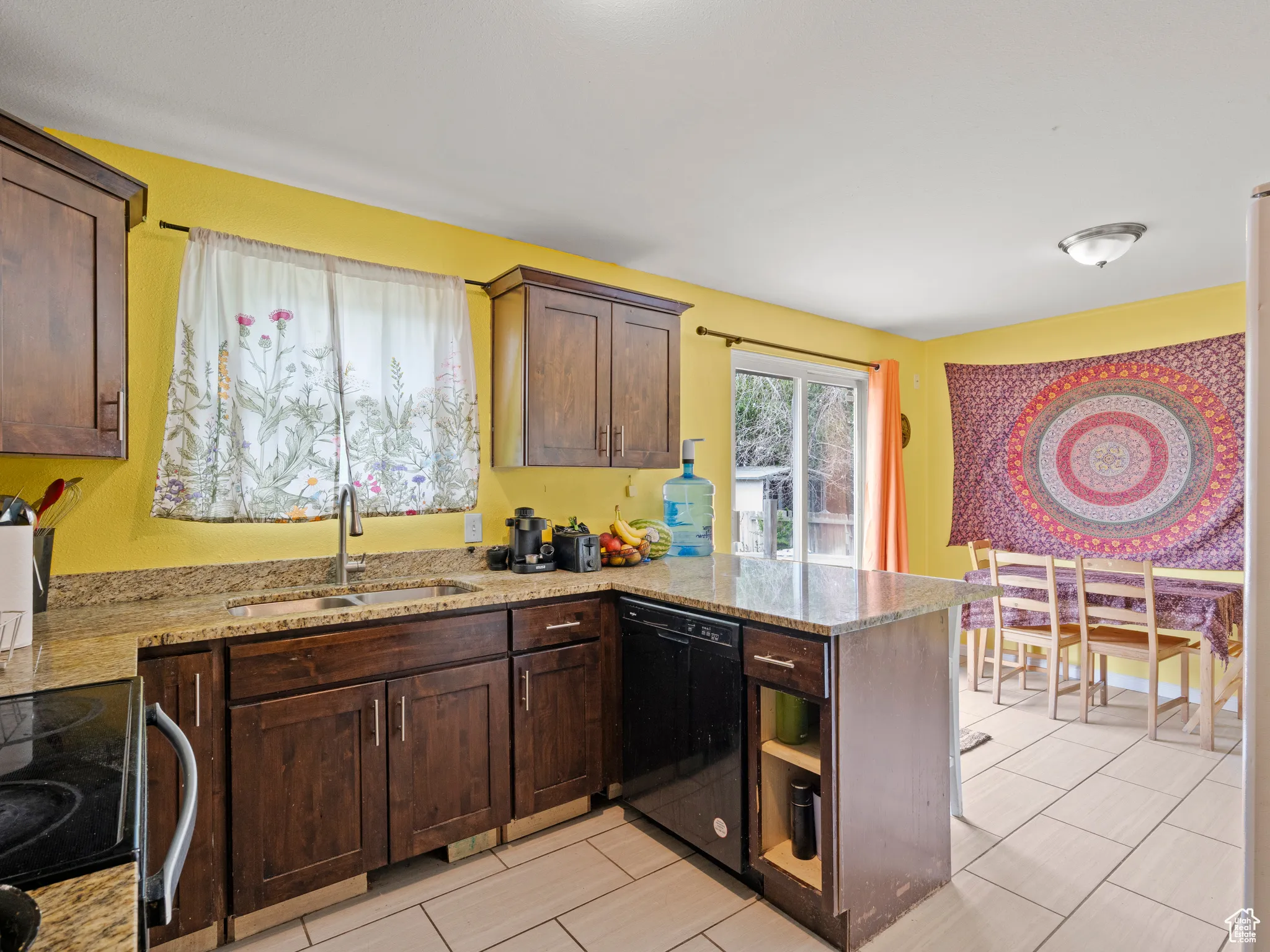 Kitchen featuring dishwasher, a peninsula, range with electric cooktop, light stone countertops, and dark brown cabinets