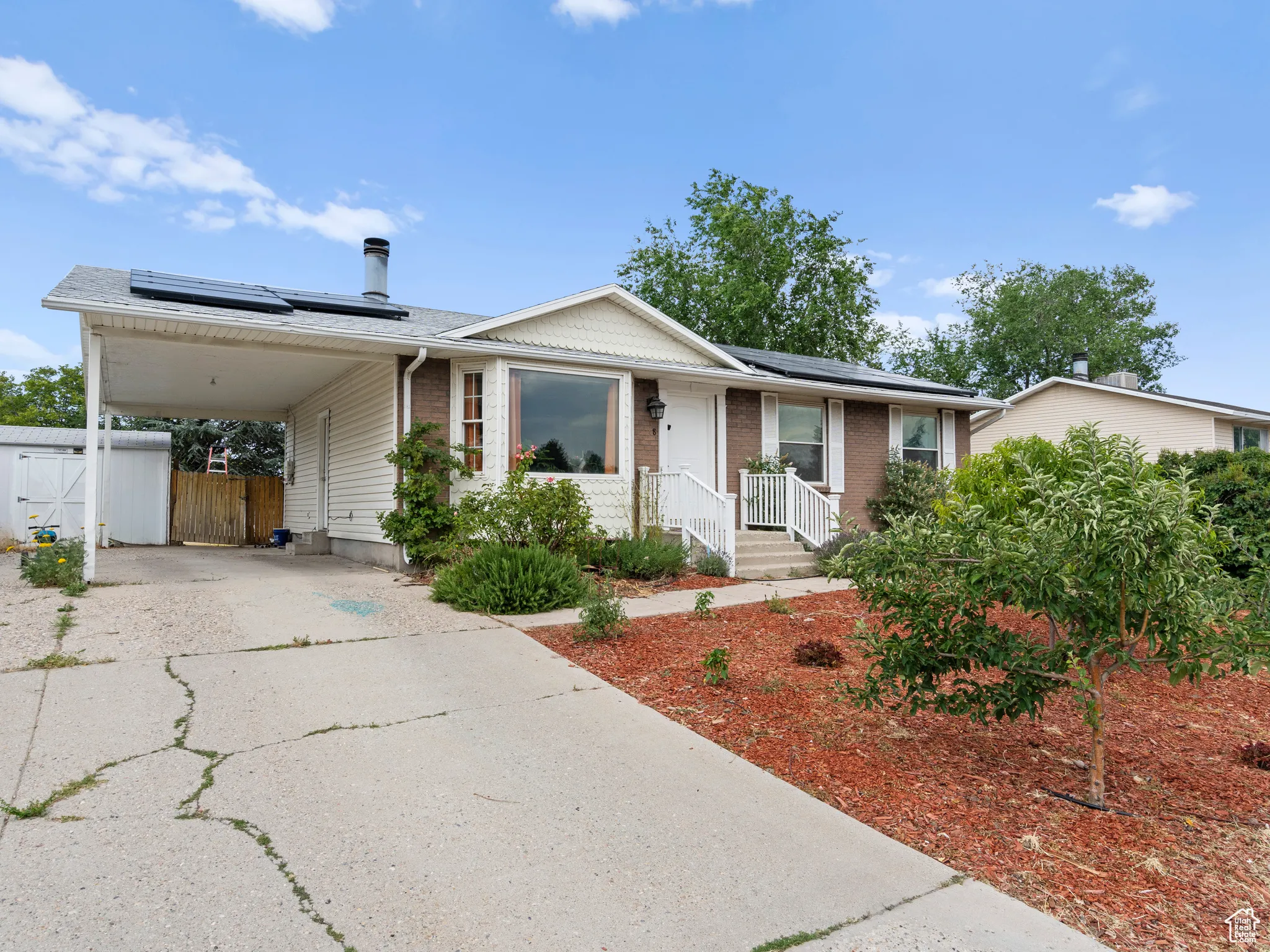 View of front of property with driveway, roof mounted solar panels, a carport, a gate, and brick siding