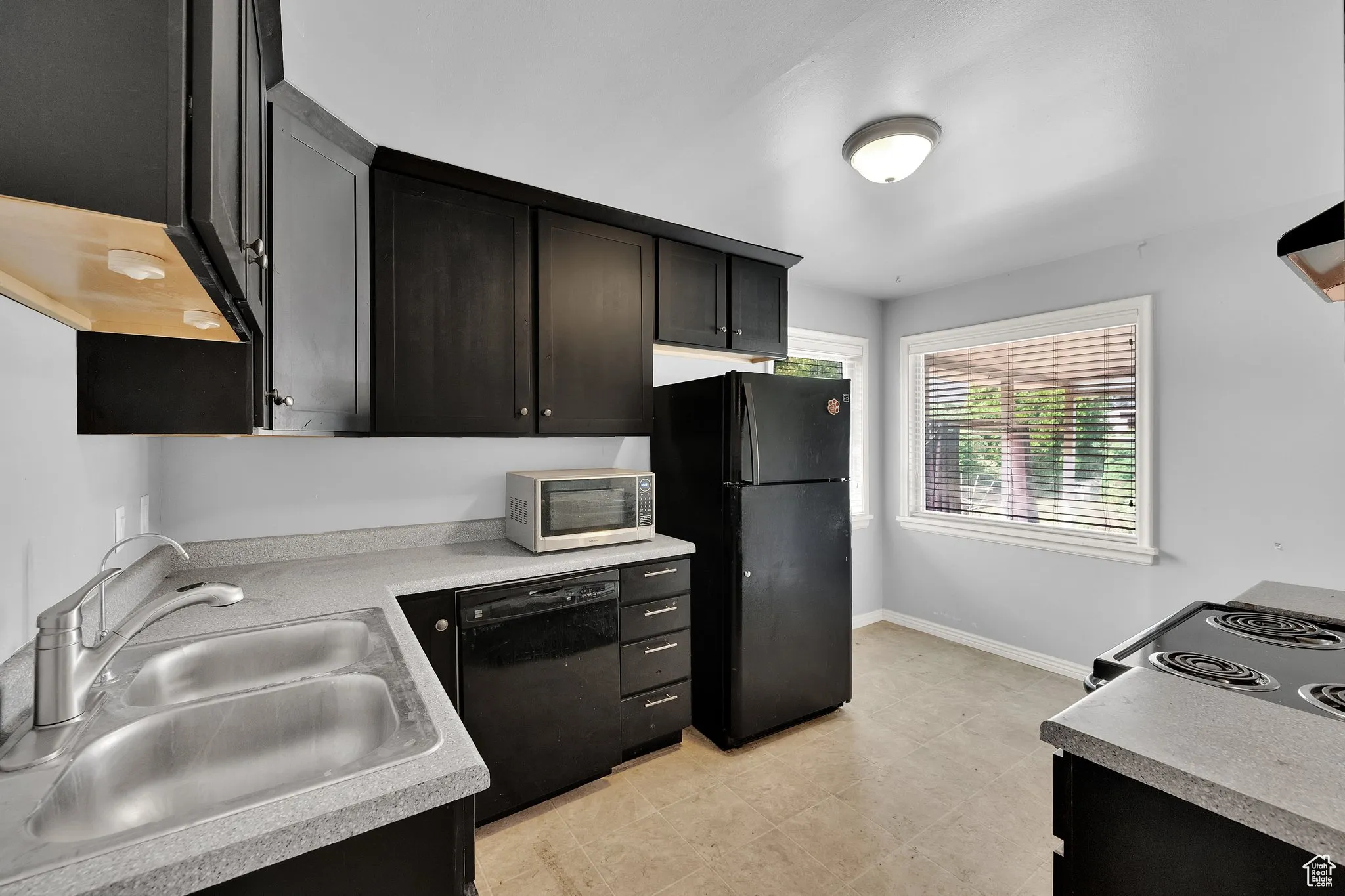 Kitchen featuring black appliances, light countertops, and dark cabinetry