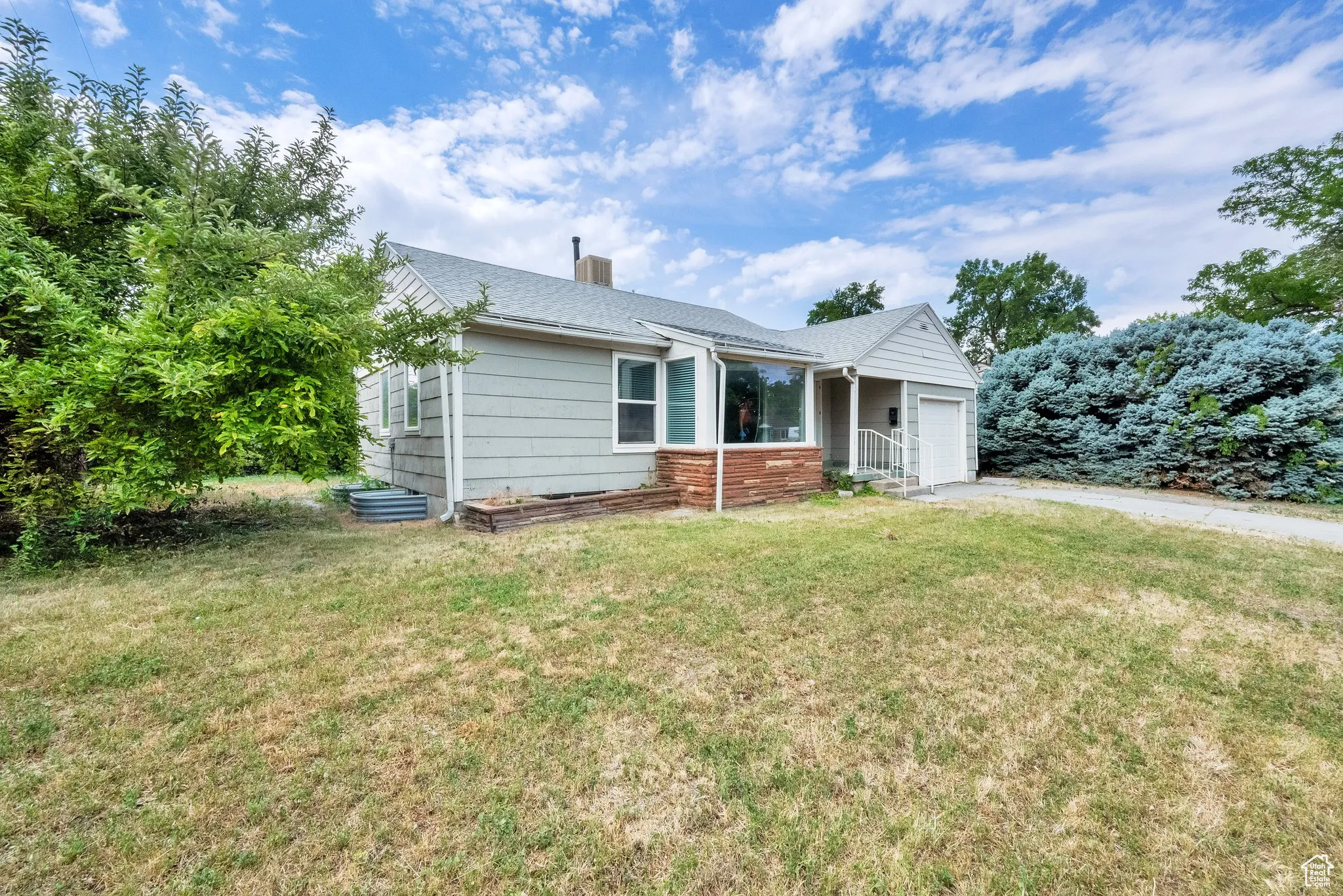 Ranch-style home featuring an attached garage, a chimney, a front lawn, driveway, and a shingled roof