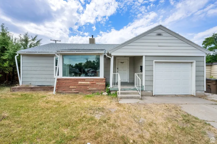 Ranch-style home with concrete driveway, an attached garage, a front lawn, a shingled roof, and a chimney