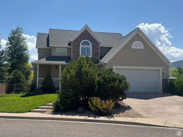 Traditional home with stone siding, driveway, an attached garage, and covered porch
