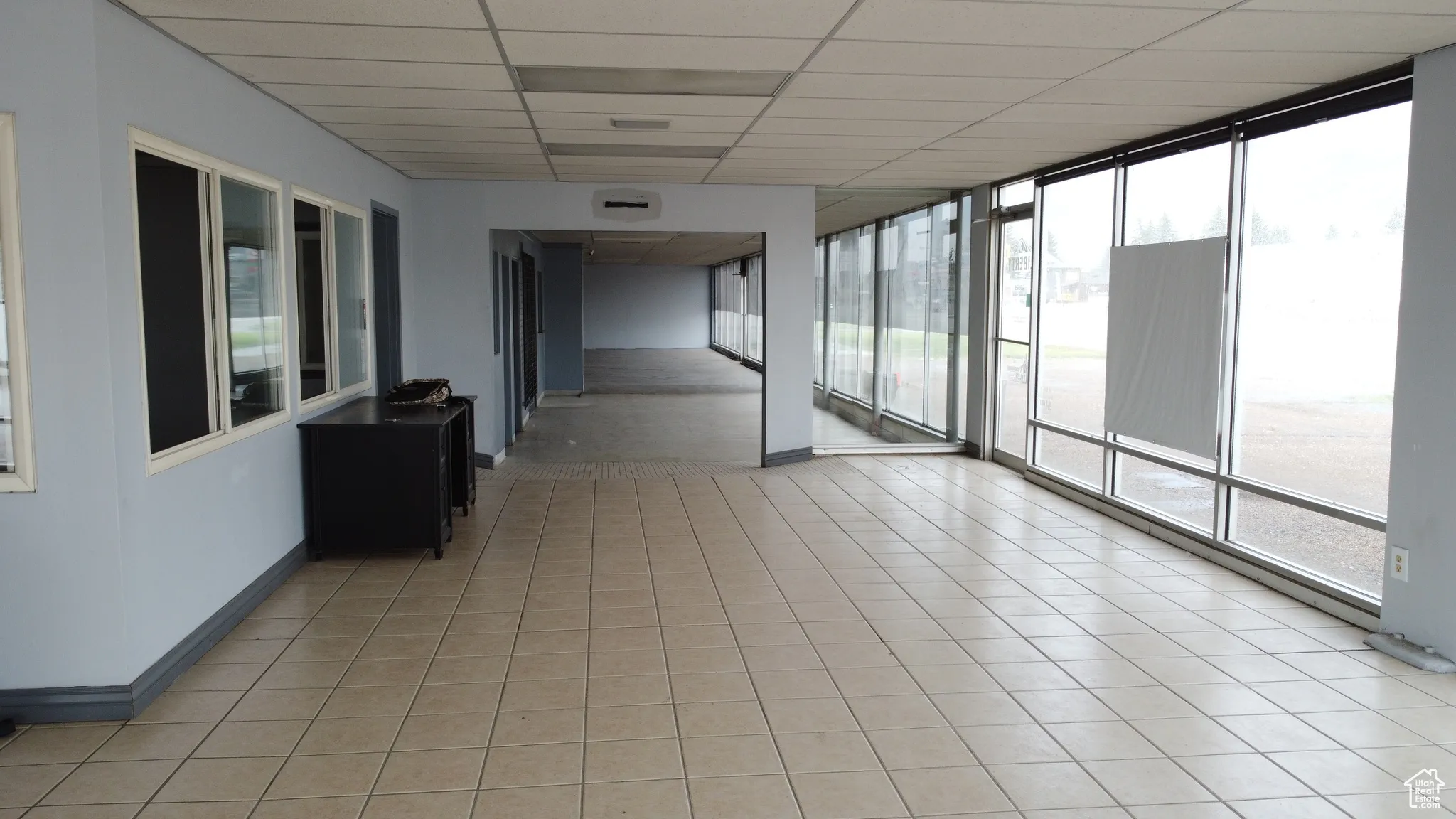 Hallway featuring a paneled ceiling, plenty of natural light, floor to ceiling windows, and light tile patterned floors