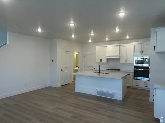 Kitchen featuring appliances with stainless steel finishes, dark wood-style flooring, white cabinets, light countertops, and recessed lighting