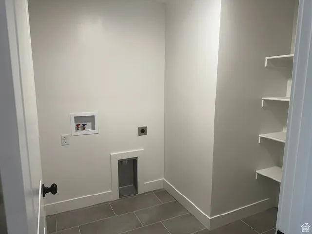 Laundry area with electric dryer hookup, hookup for a washing machine, and dark tile patterned flooring