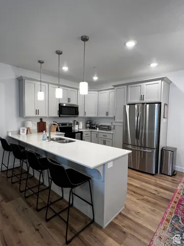 Kitchen with stainless steel appliances, a peninsula, a breakfast bar area, dark wood finished floors, and light countertops
