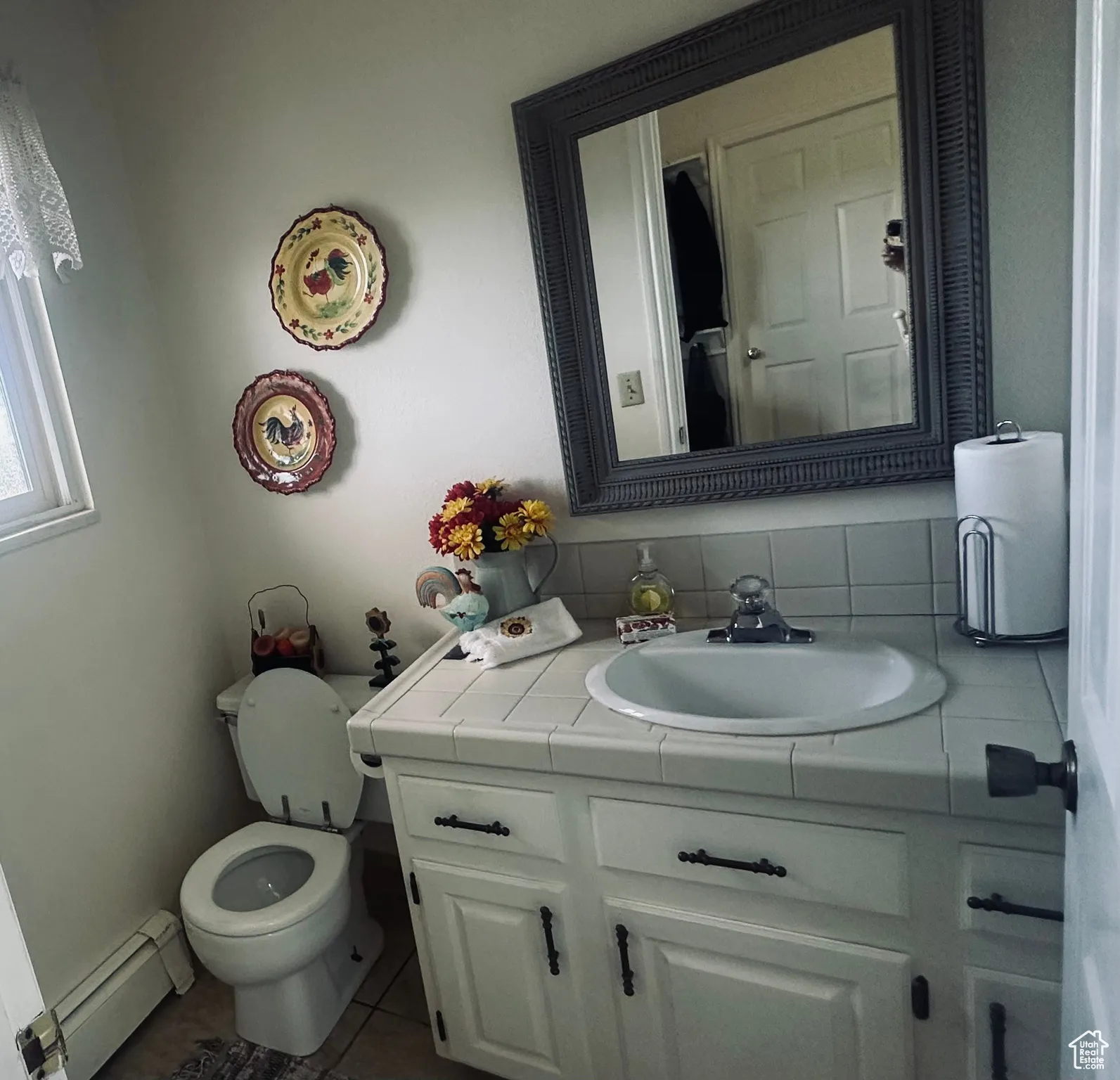 Half bathroom featuring a baseboard radiator, vanity, tile patterned floors, and backsplash
