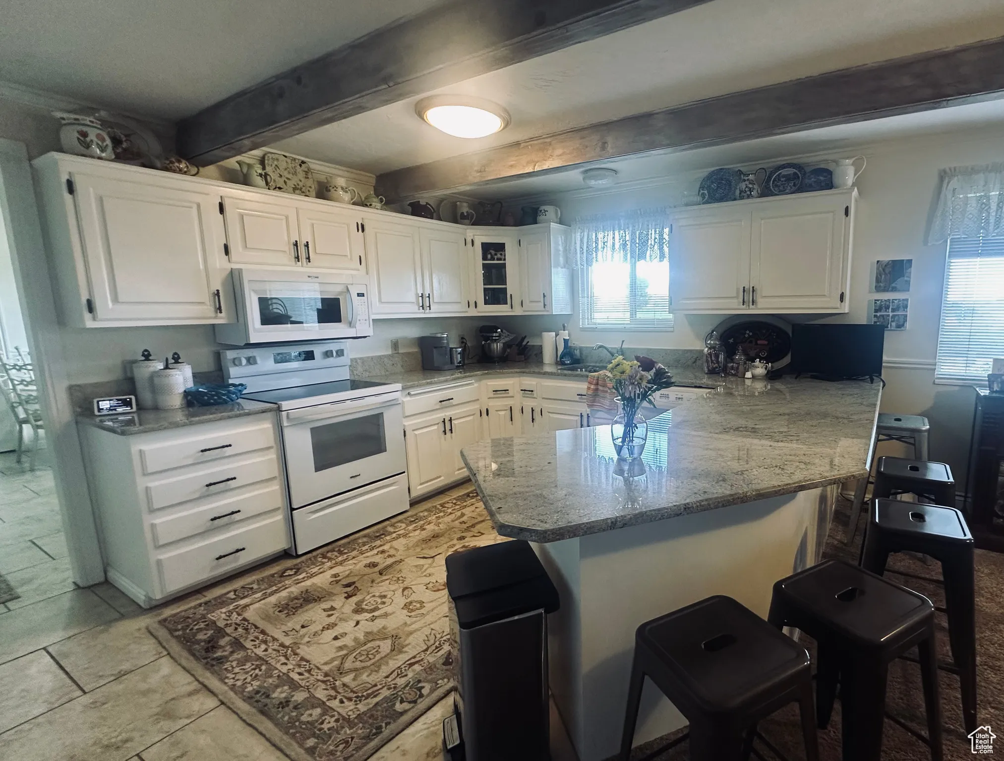 Kitchen with white appliances, a peninsula, a kitchen bar, white cabinetry, and light stone countertops