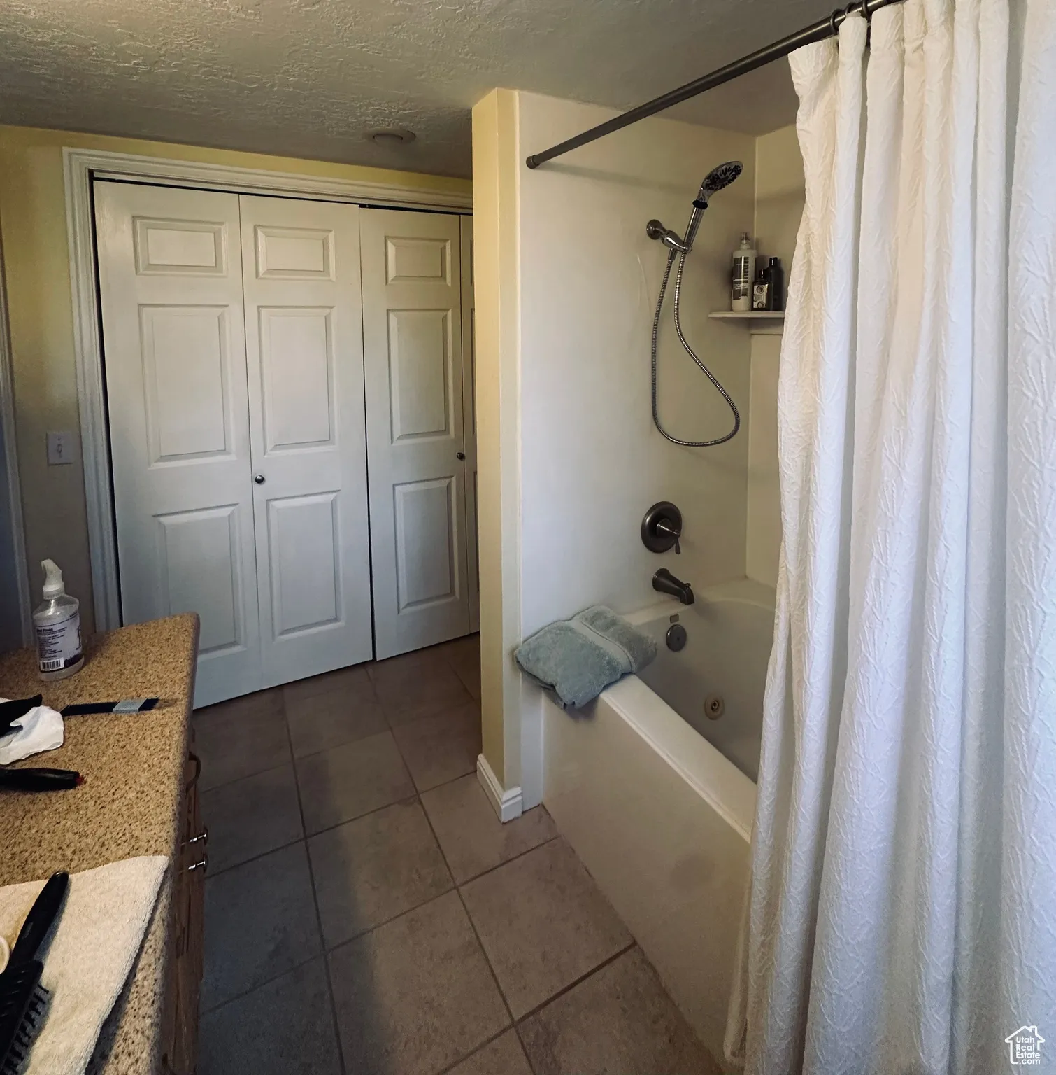 Full bath with tile patterned flooring, shower / bath combination with curtain, vanity, and a textured ceiling