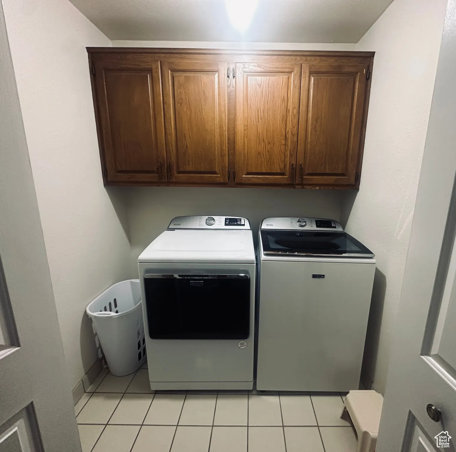Laundry area with independent washer and dryer, light tile patterned flooring, and cabinet space