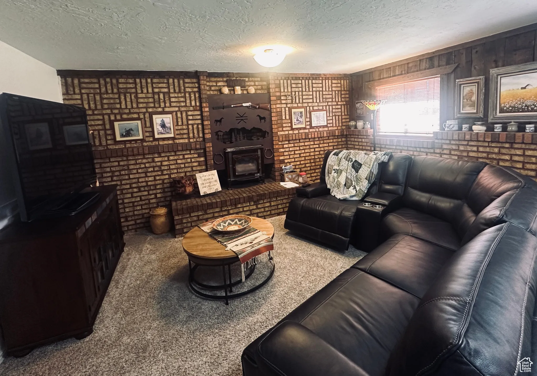 Living room with a wood stove, a textured ceiling, brick wall, carpet floors, and wood walls