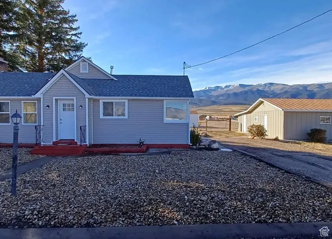 Ranch-style home with a mountain view, roof with shingles, and gravel driveway