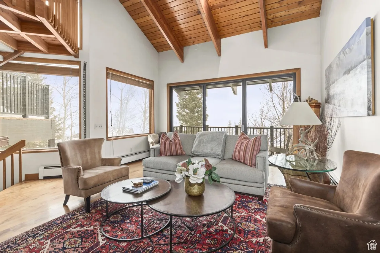 Living area with a baseboard radiator, a wood ceiling with exposed beams, wood finished floors, and high vaulted ceiling