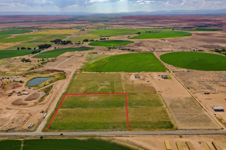 Expansive undeveloped land parcel featuring a visible red-lined boundary, direct paved road frontage, and surrounding agricultural fields