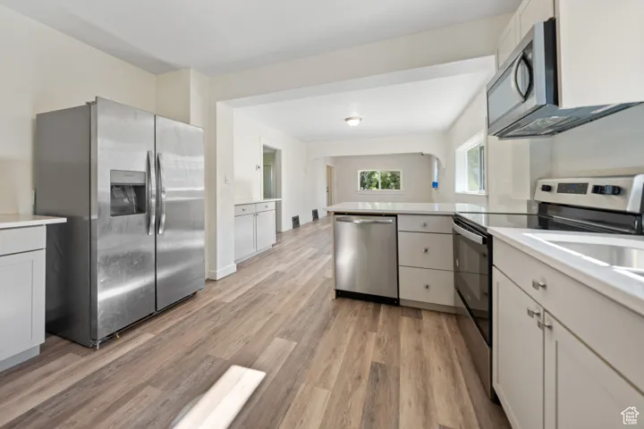 Kitchen with appliances with stainless steel finishes, a peninsula, light wood finished floors, and light countertops