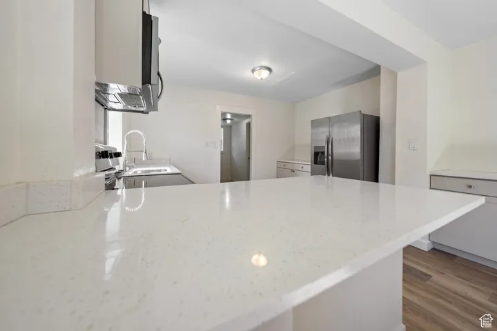 Kitchen featuring stainless steel fridge, a peninsula, light stone countertops, and wood finished floors