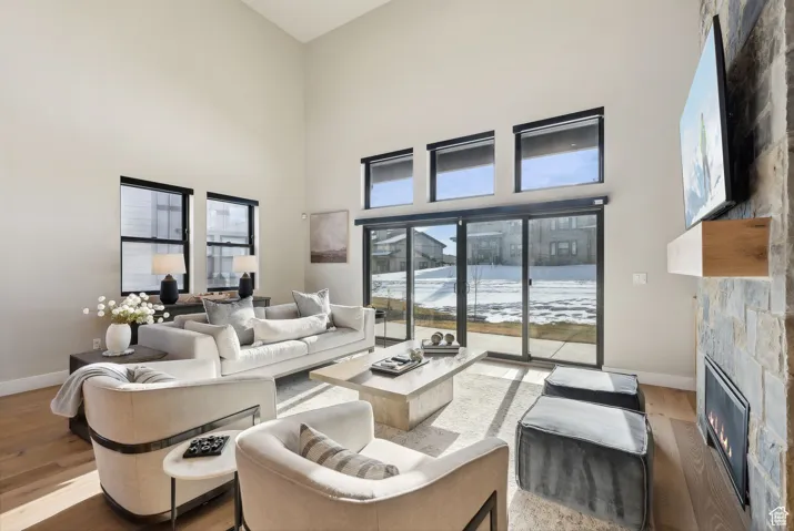Living area with a glass covered fireplace, wood finished floors, and a high ceiling