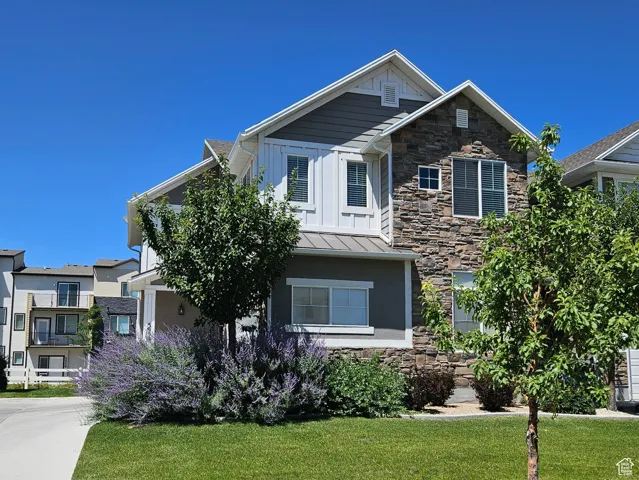 Craftsman inspired home featuring stone siding, a front lawn, and a standing seam roof