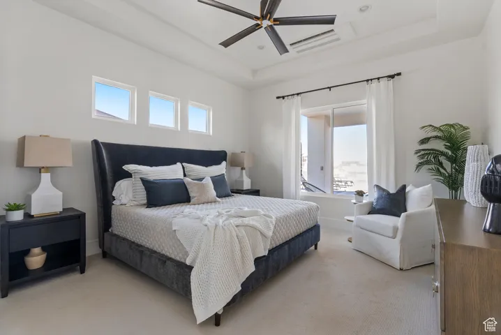 Bedroom featuring a tray ceiling, light colored carpet, and a ceiling fan