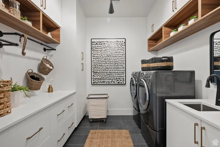 Laundry area featuring separate washer and dryer, cabinet space, and dark tile patterned floors