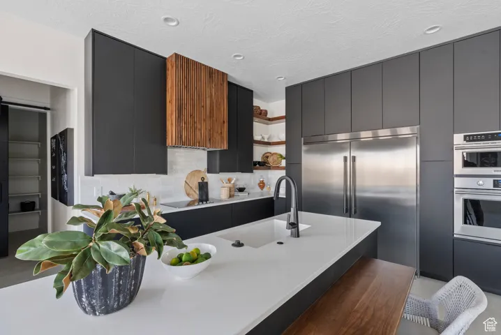 Kitchen featuring open shelves, modern cabinets, appliances with stainless steel finishes, and dark cabinetry