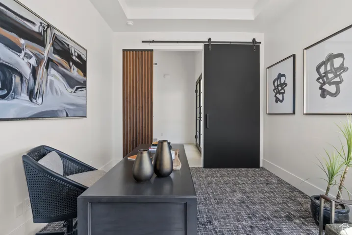Carpeted home office with a barn door and a tray ceiling