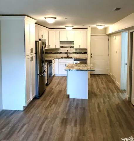 Kitchen with appliances with stainless steel finishes, light stone countertops, white cabinetry, dark wood-style floors, and backsplash