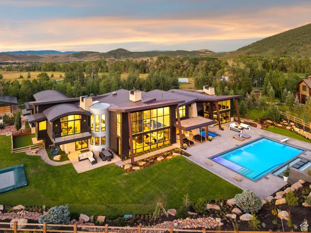 Back of house at dusk with an outdoor living space, a chimney, a balcony, a fenced backyard, and a patio
