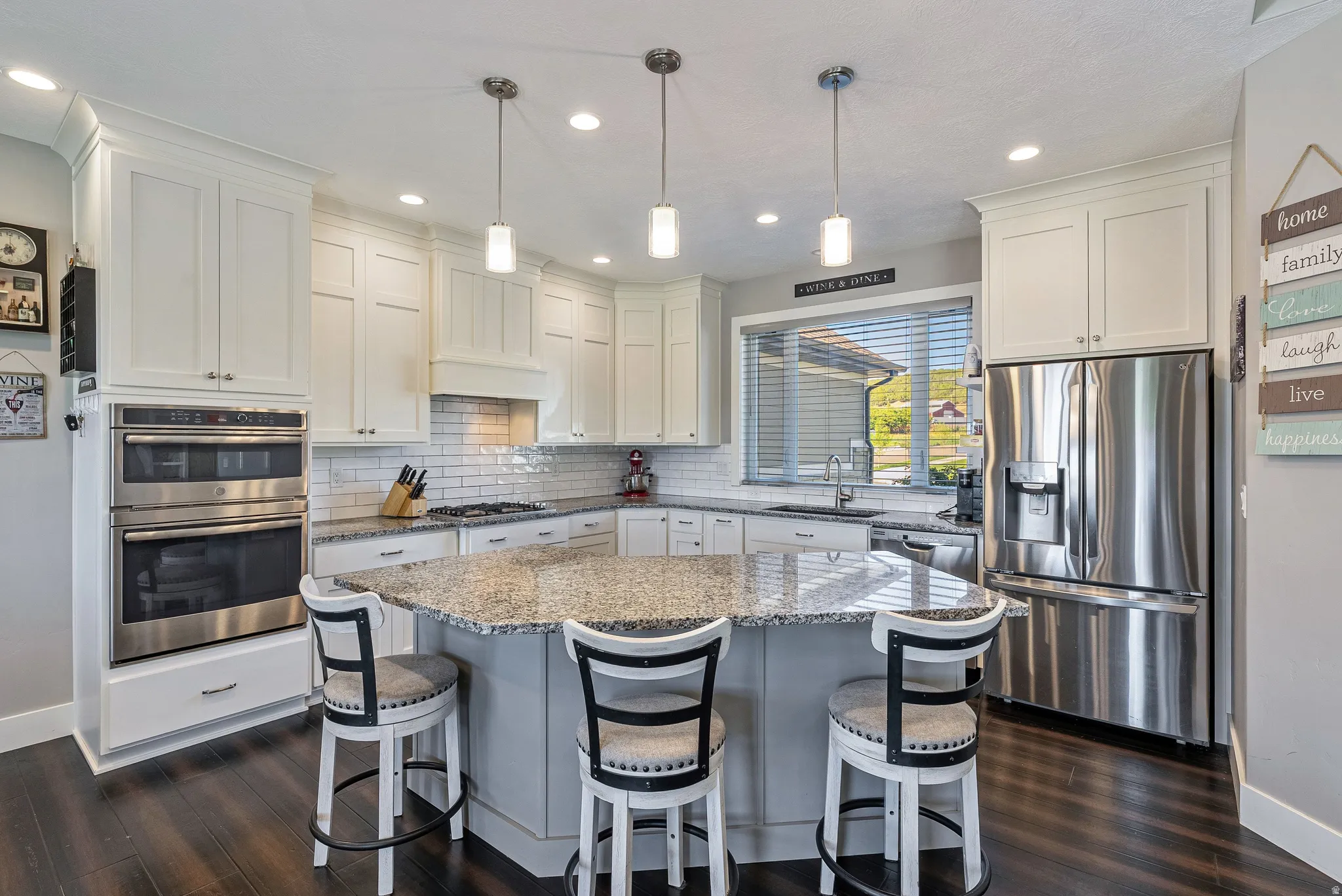 Kitchen featuring a granite-topped island with seating, white shaker cabinetry, stainless steel double wall ovens, a stainless steel refrigerator, and dark wood-finish flooring