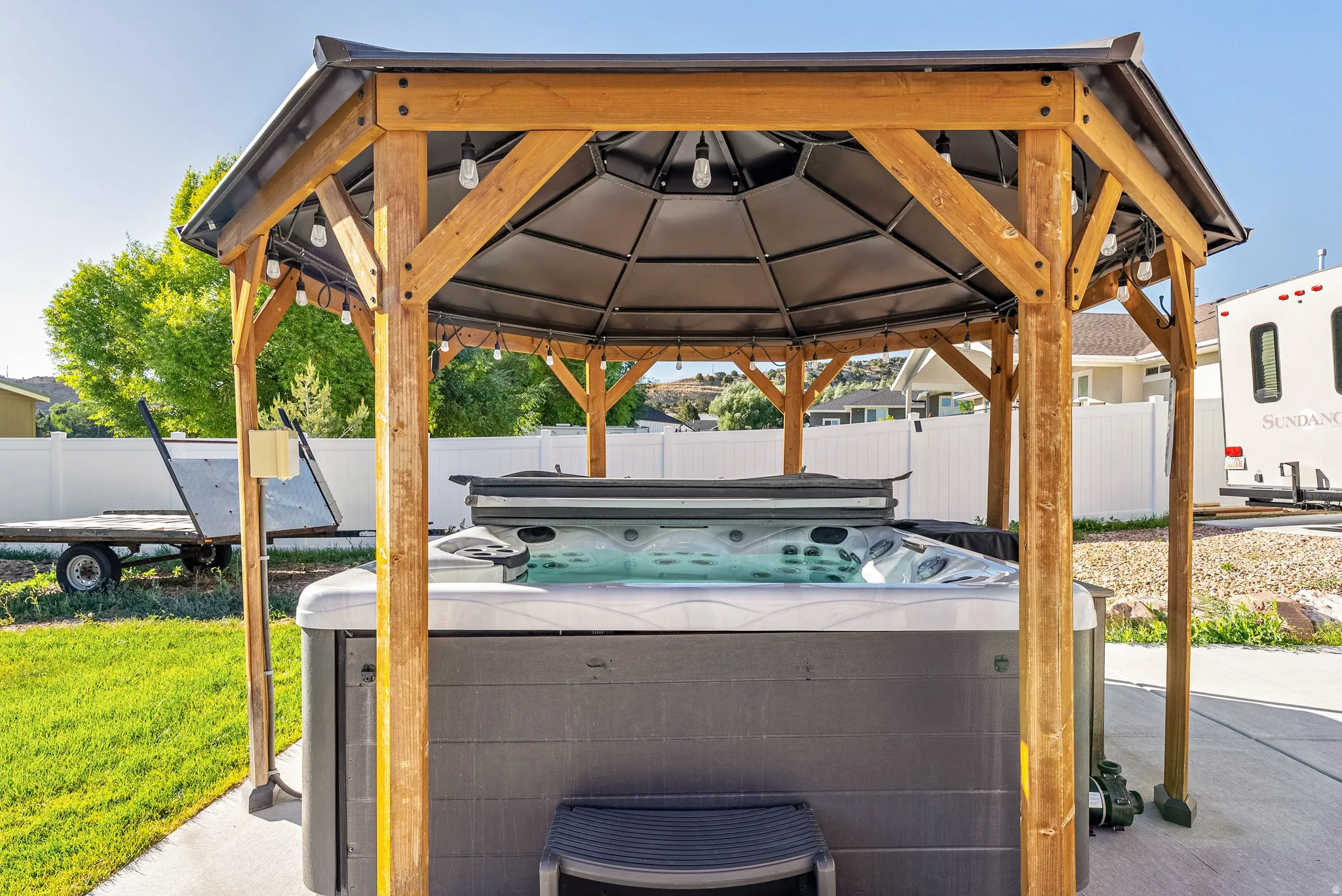 Outdoor hot tub set within a wood-frame gazebo, featuring a dark canopy and string lighting