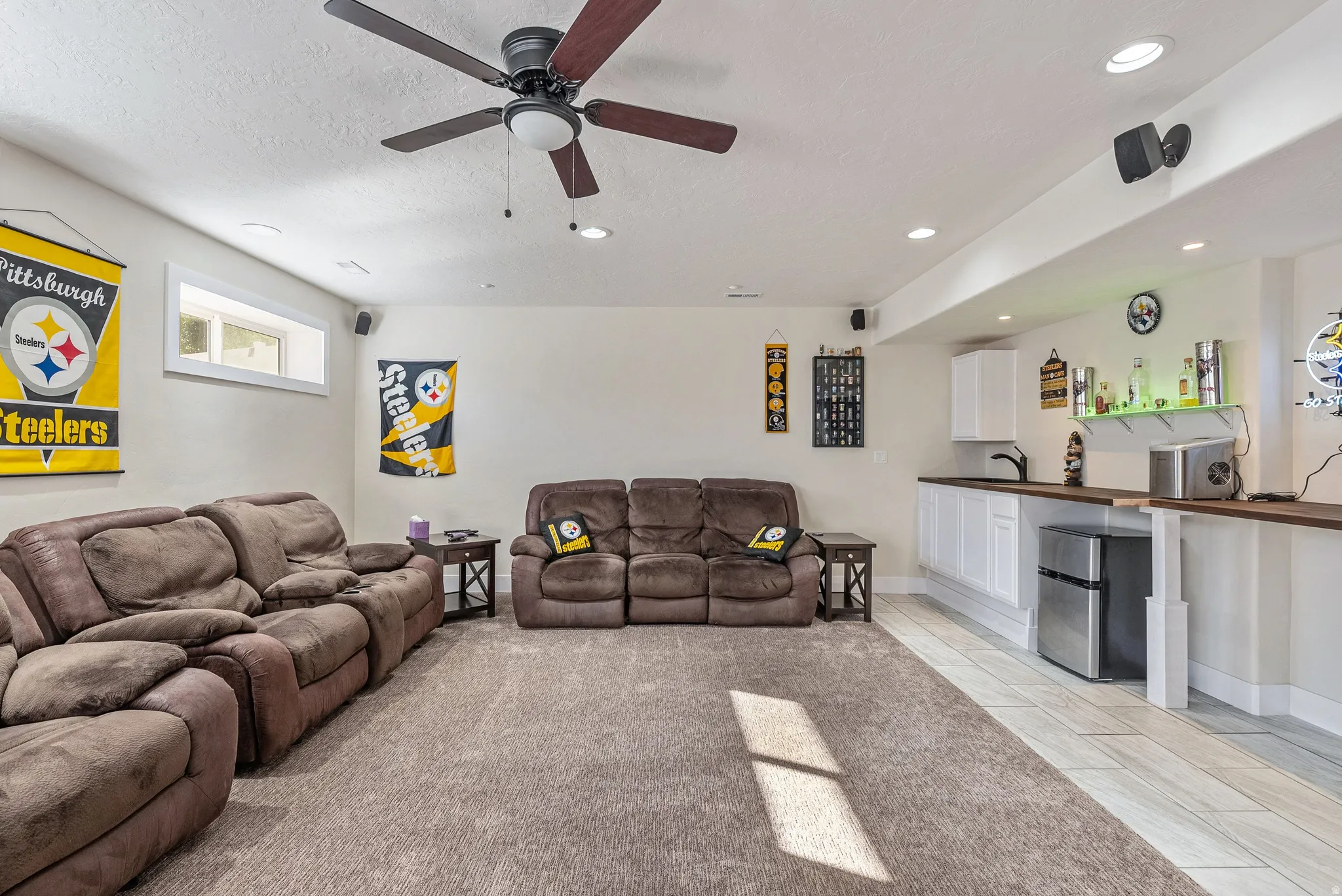 Versatile recreation room featuring a built-in wet bar with a stainless steel mini-fridge, wood-finish countertop, and white cabinetry