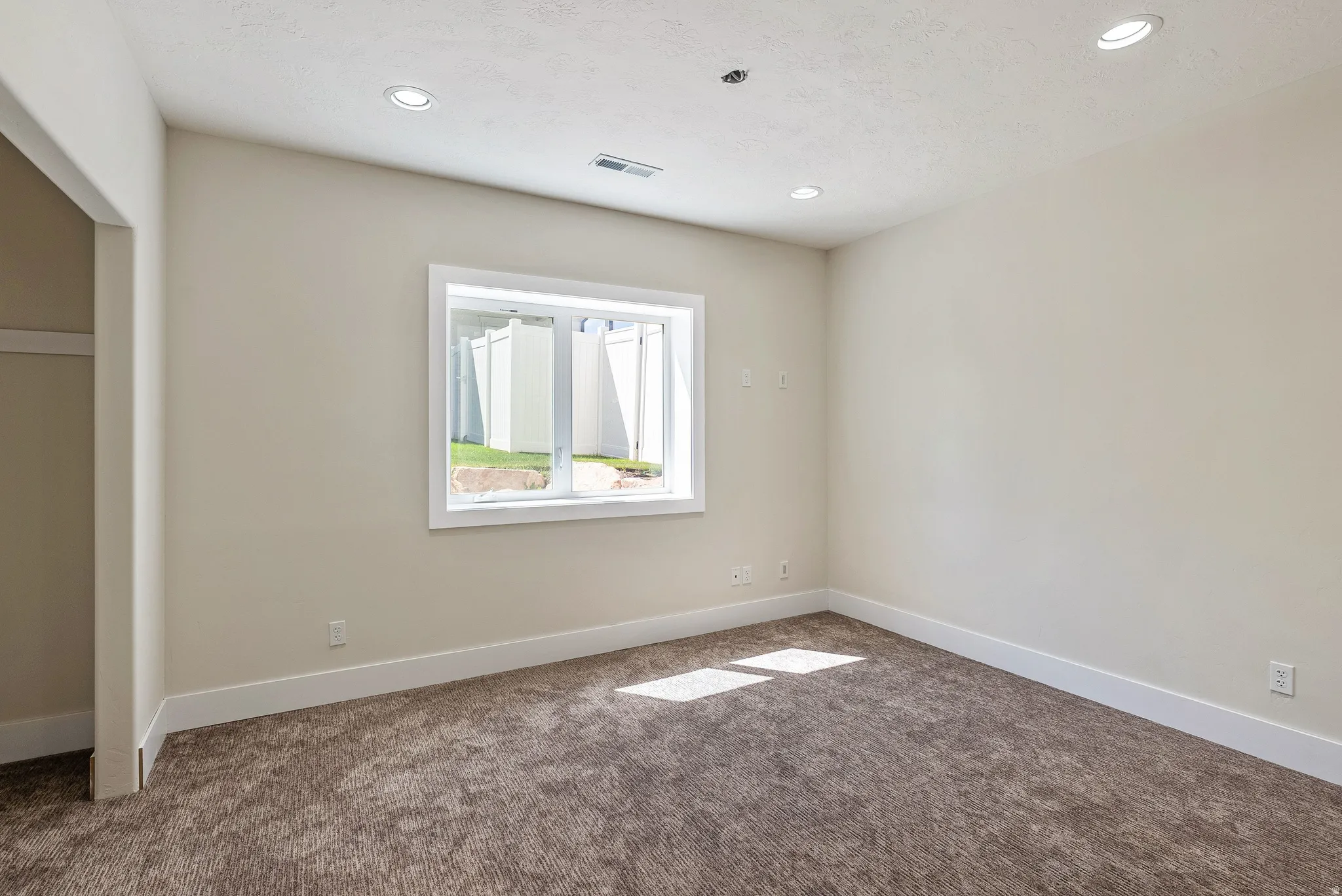 Neutral-toned room with plush carpet flooring, recessed lighting, and a white-framed window