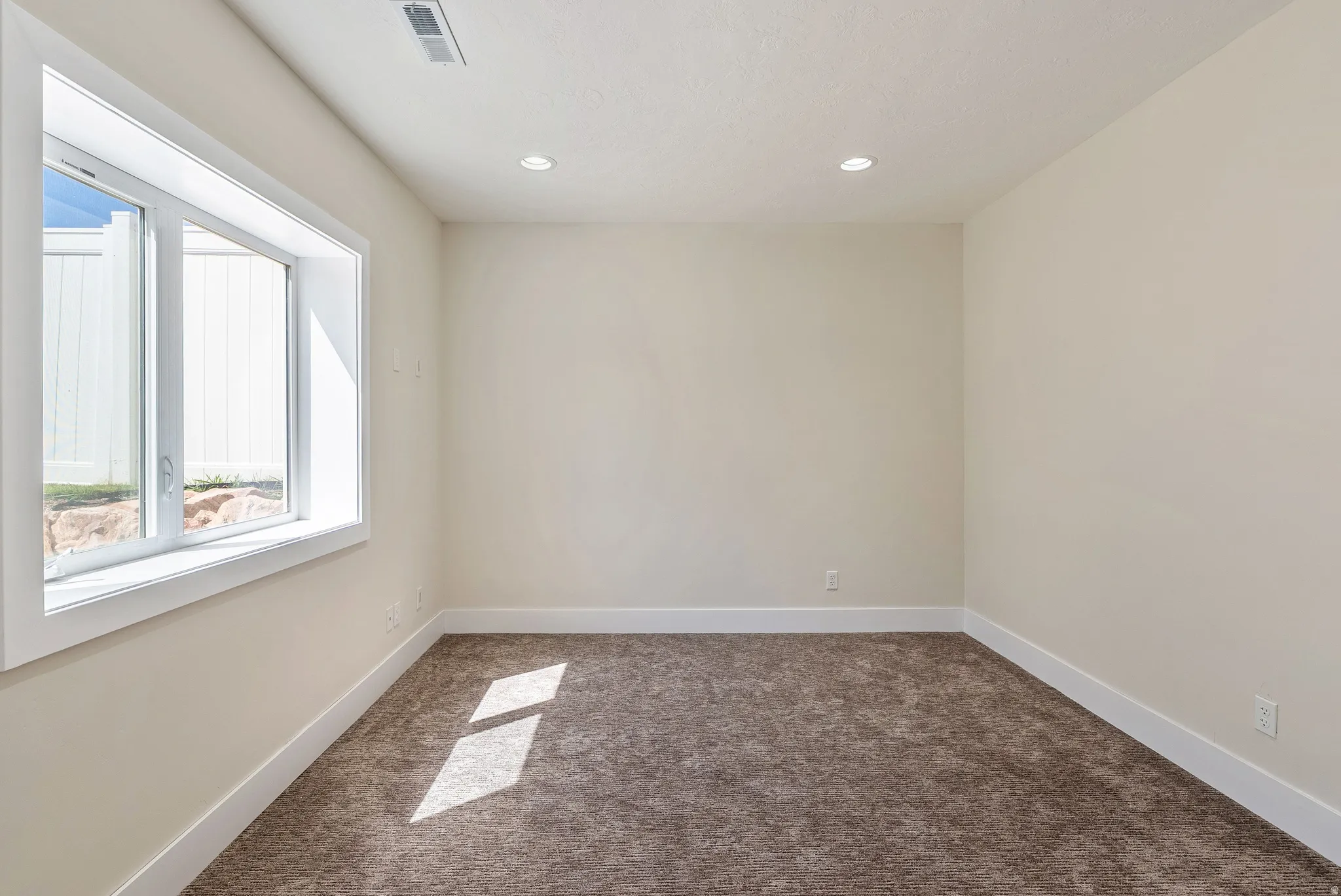 Carpeted room featuring a large egress window with white trim, recessed lighting, and light-toned walls