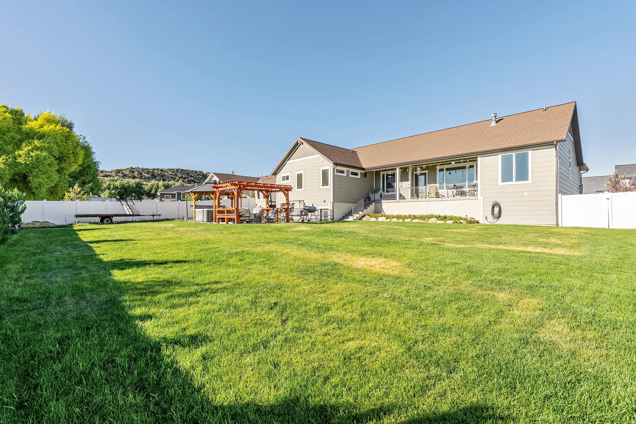 Expansive backyard featuring a large green lawn, a covered patio, and a separate wood pergola with a stone base