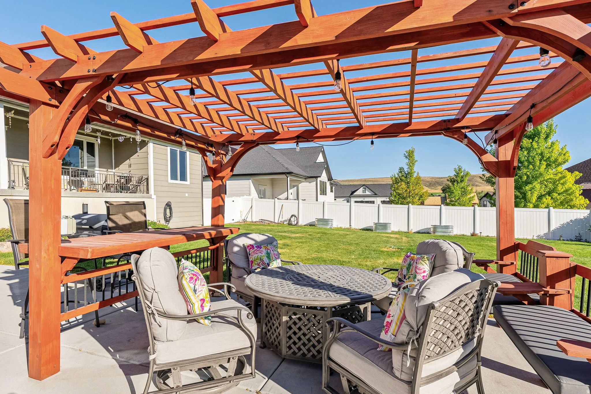 Patio area featuring a wood pergola with integrated string lighting, concrete flooring, and a manicured lawn