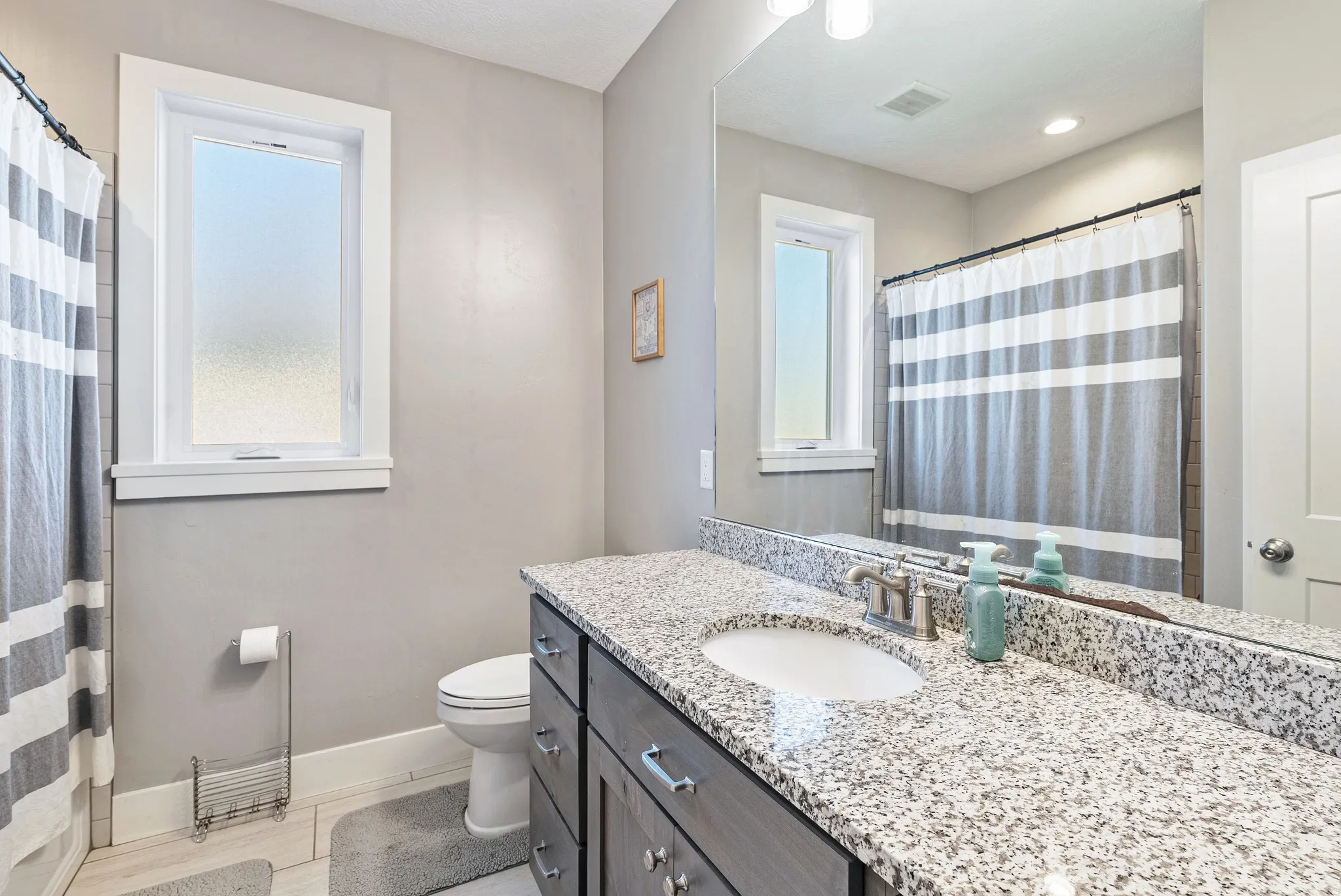 Bathroom vanity featuring a speckled countertop, undermount sink, and wood-finish cabinetry with silver hardware