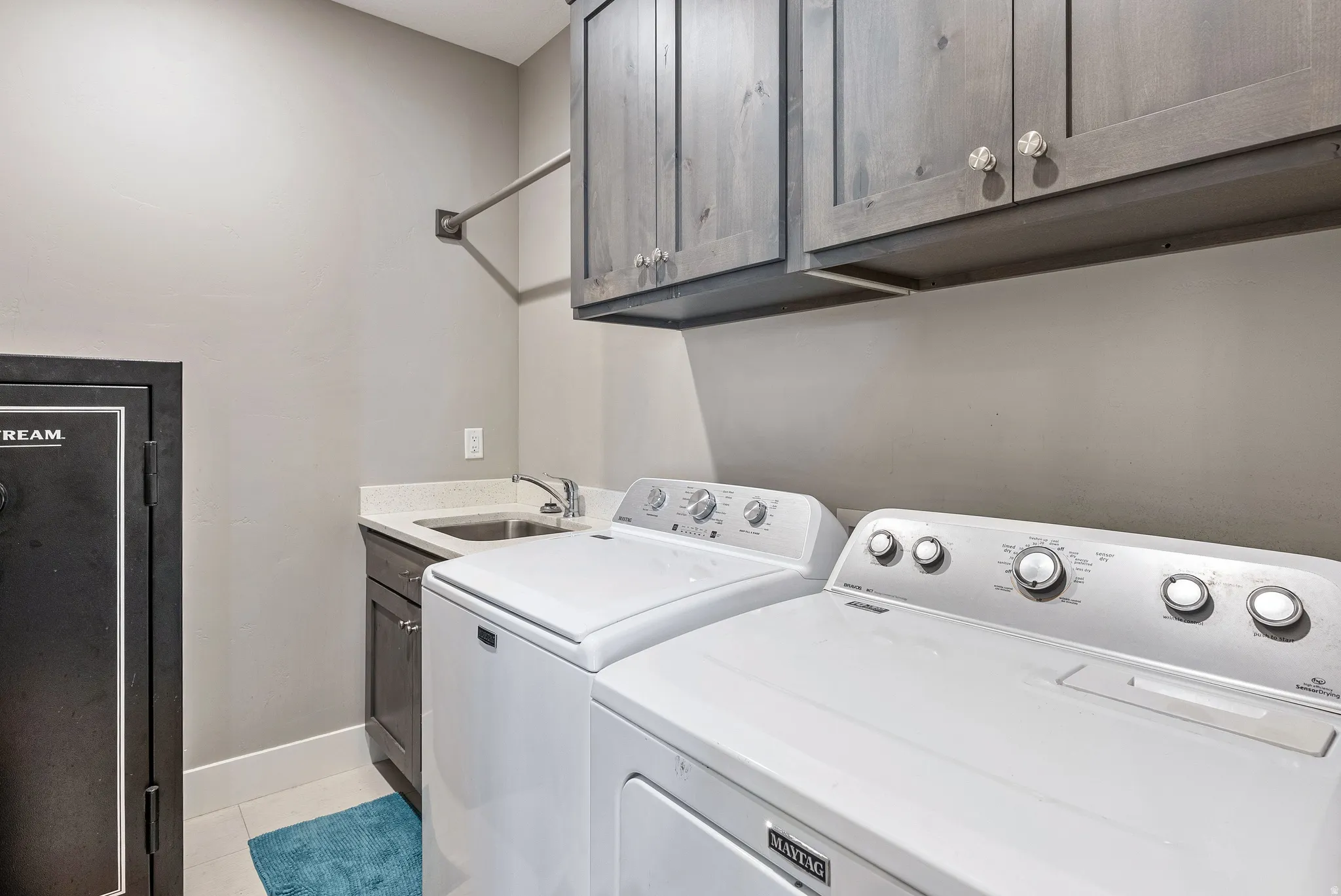 Laundry area featuring upper cabinetry with decorative hardware, a utility sink with a stone-finish countertop, and a clothes hanging rod