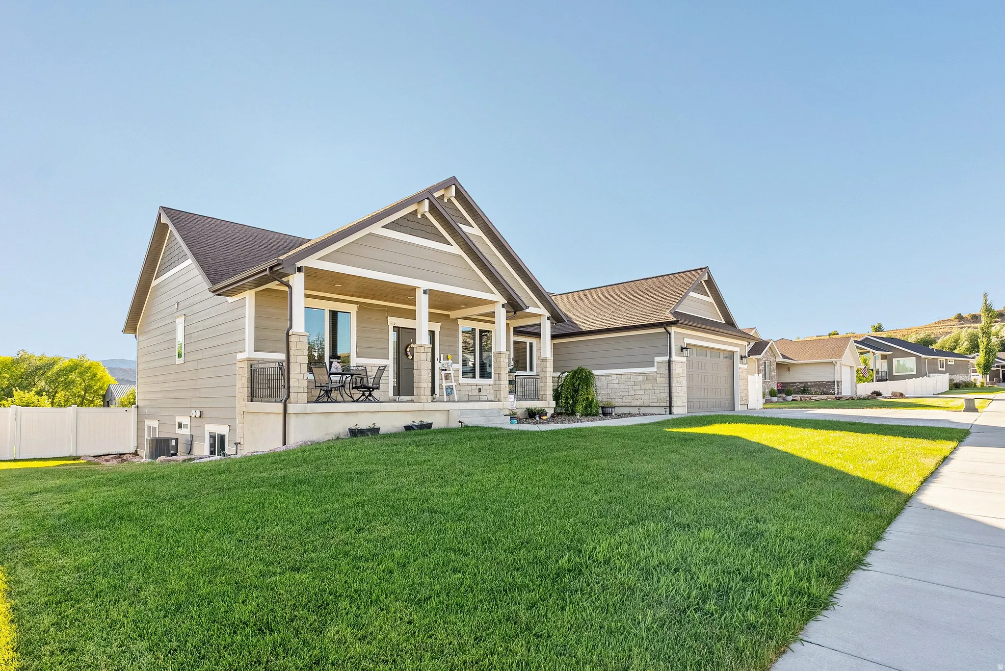 Contemporary ranch-style residence featuring a covered front porch with stone accents, a two-car garage, and a manicured front lawn