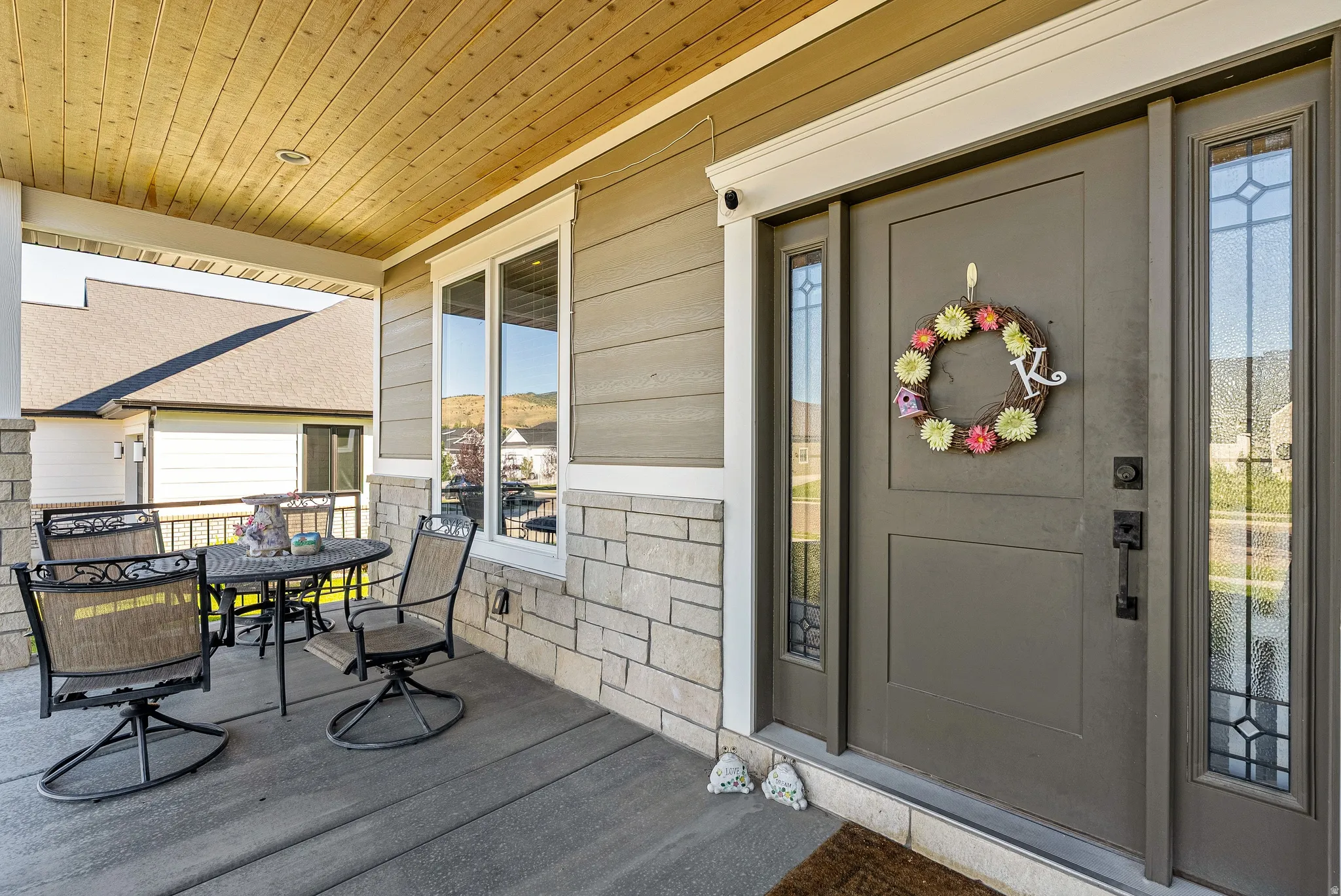 Covered front porch featuring a wood-finish ceiling, stone veneer accents, and a grey plank-style floor