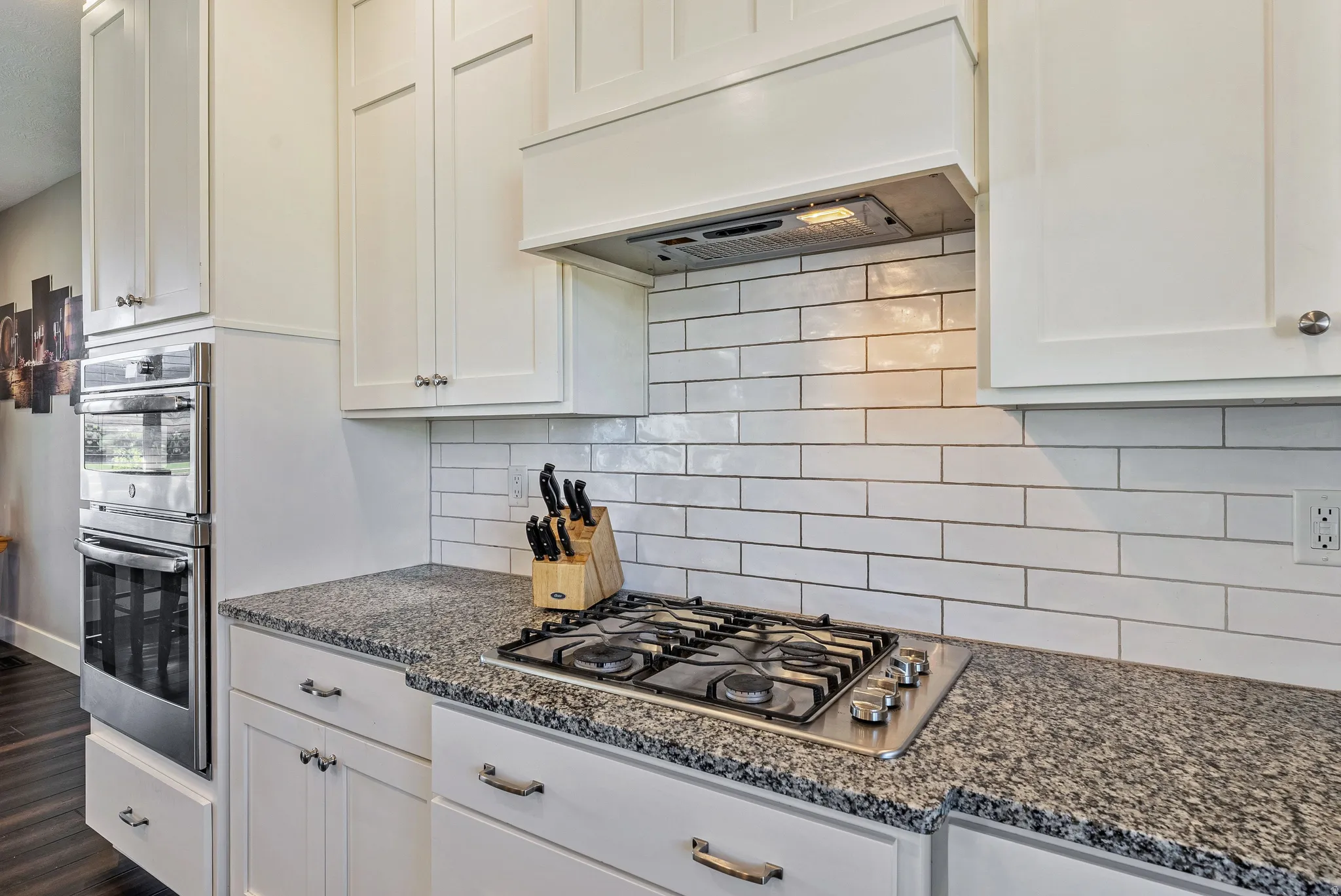 Kitchen featuring white shaker-style cabinetry, a gas cooktop, granite countertops, and a subway tile backsplash
