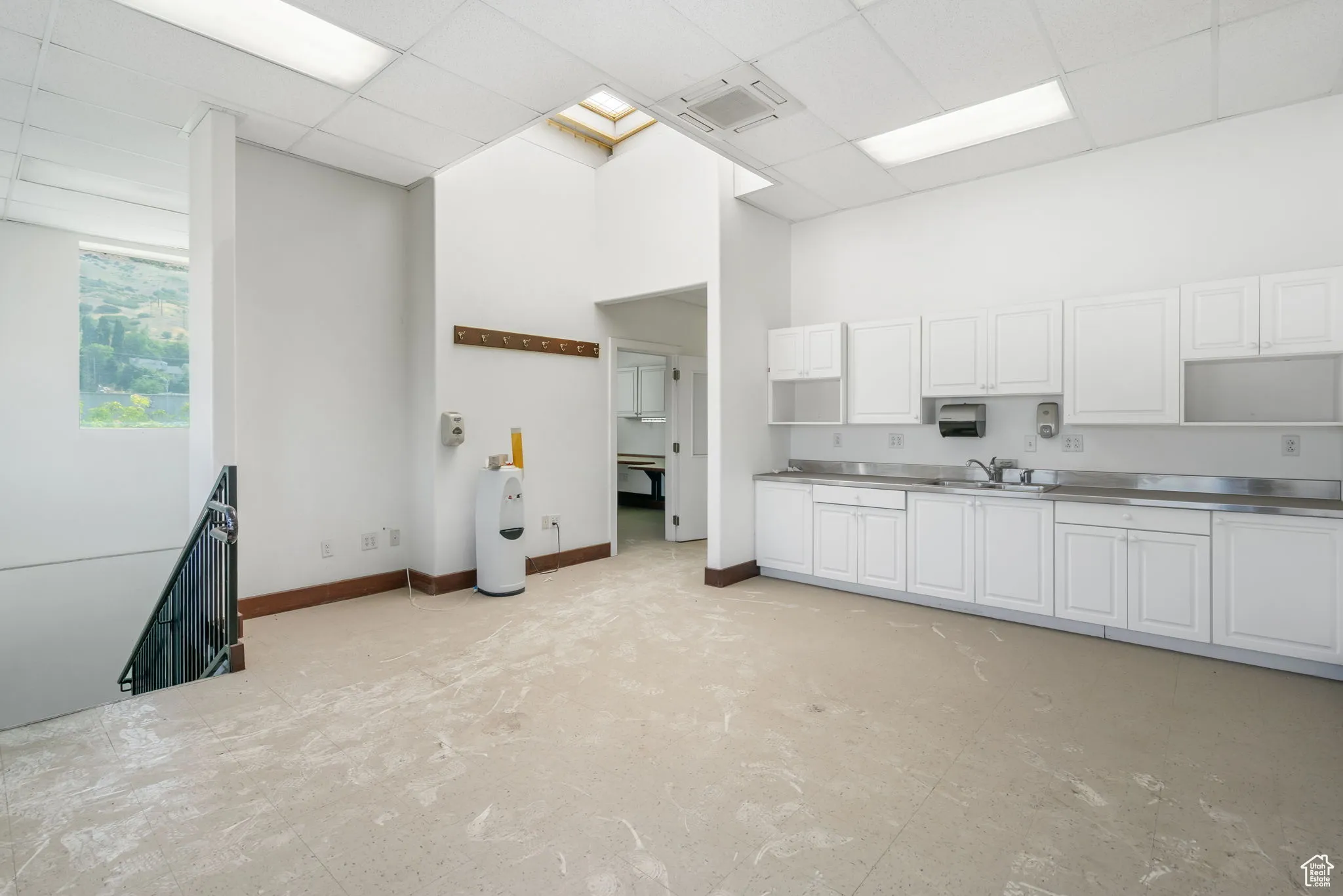 Kitchen with stainless steel counters, a drop ceiling, a towering ceiling, and white cabinets