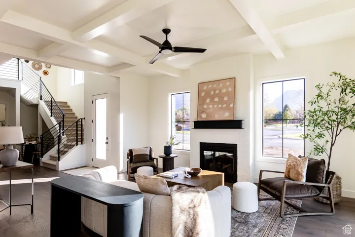 Living room featuring coffered ceiling, plenty of natural light, a fireplace, wood finished floors, and beamed ceiling