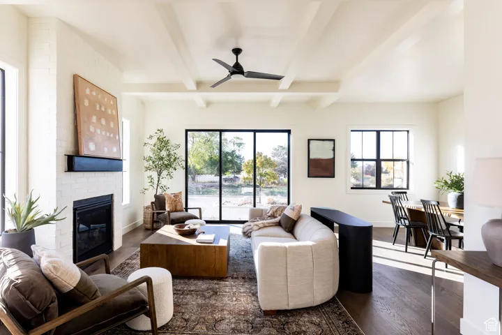 Living area with dark wood-type flooring, a ceiling fan, a fireplace, and beamed ceiling