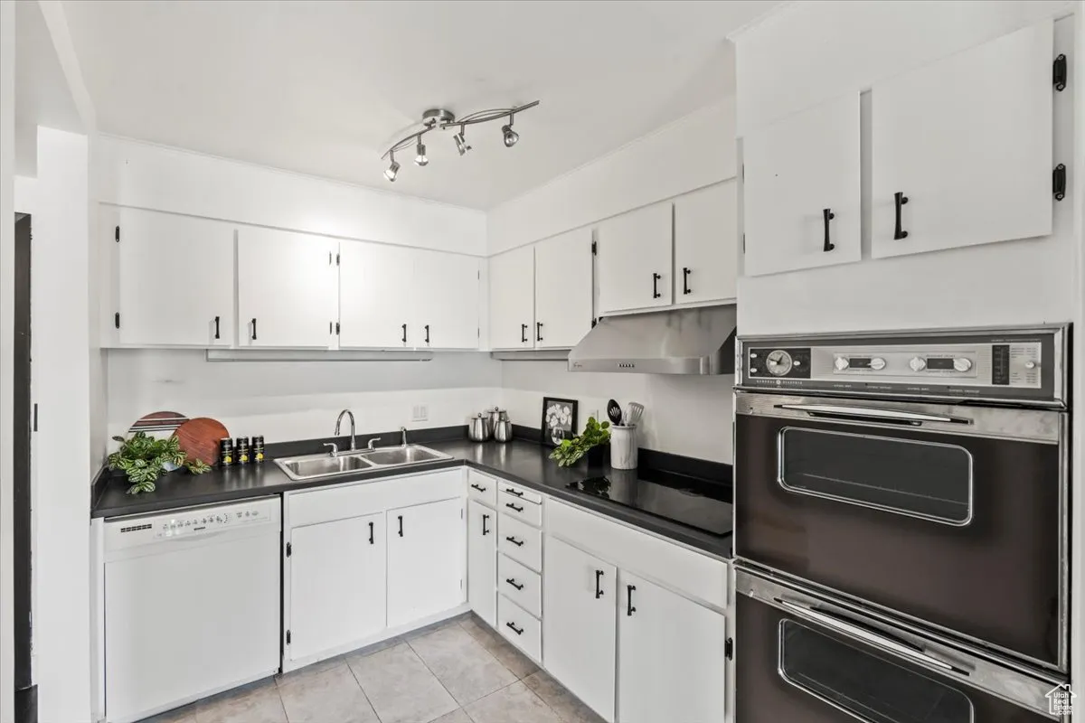 Kitchen with black appliances, dark countertops, light tile patterned floors, white cabinetry, and under cabinet range hood