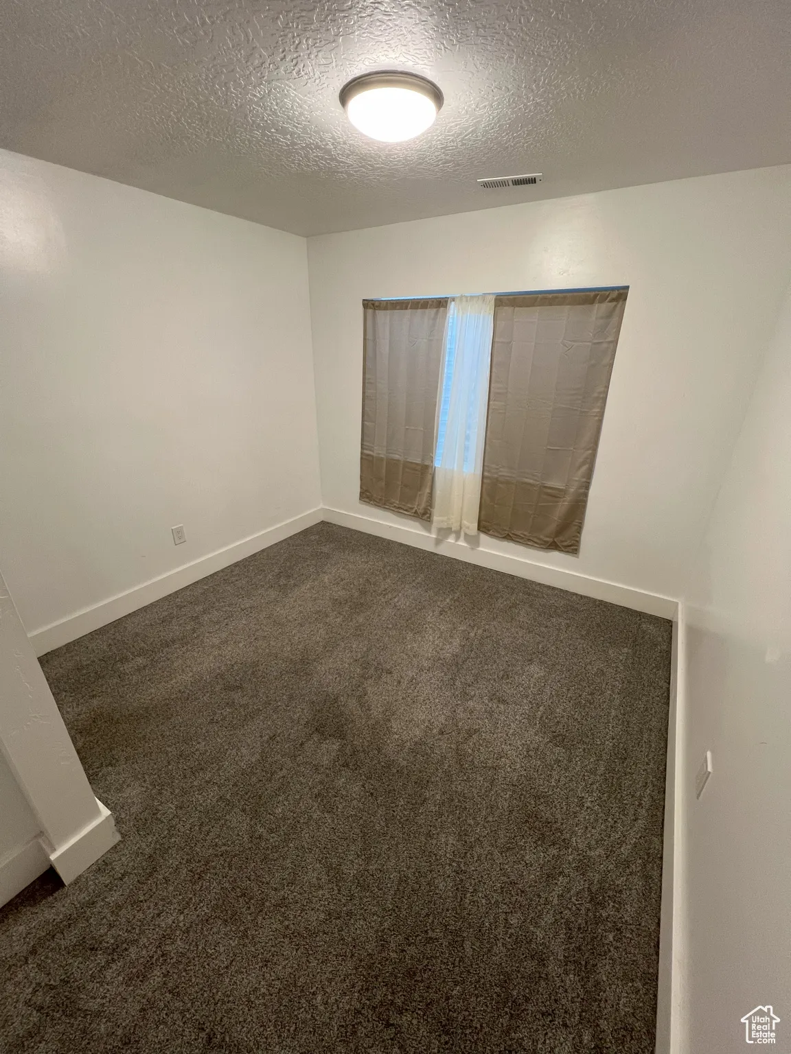 Unfurnished room with dark colored carpet and a textured ceiling