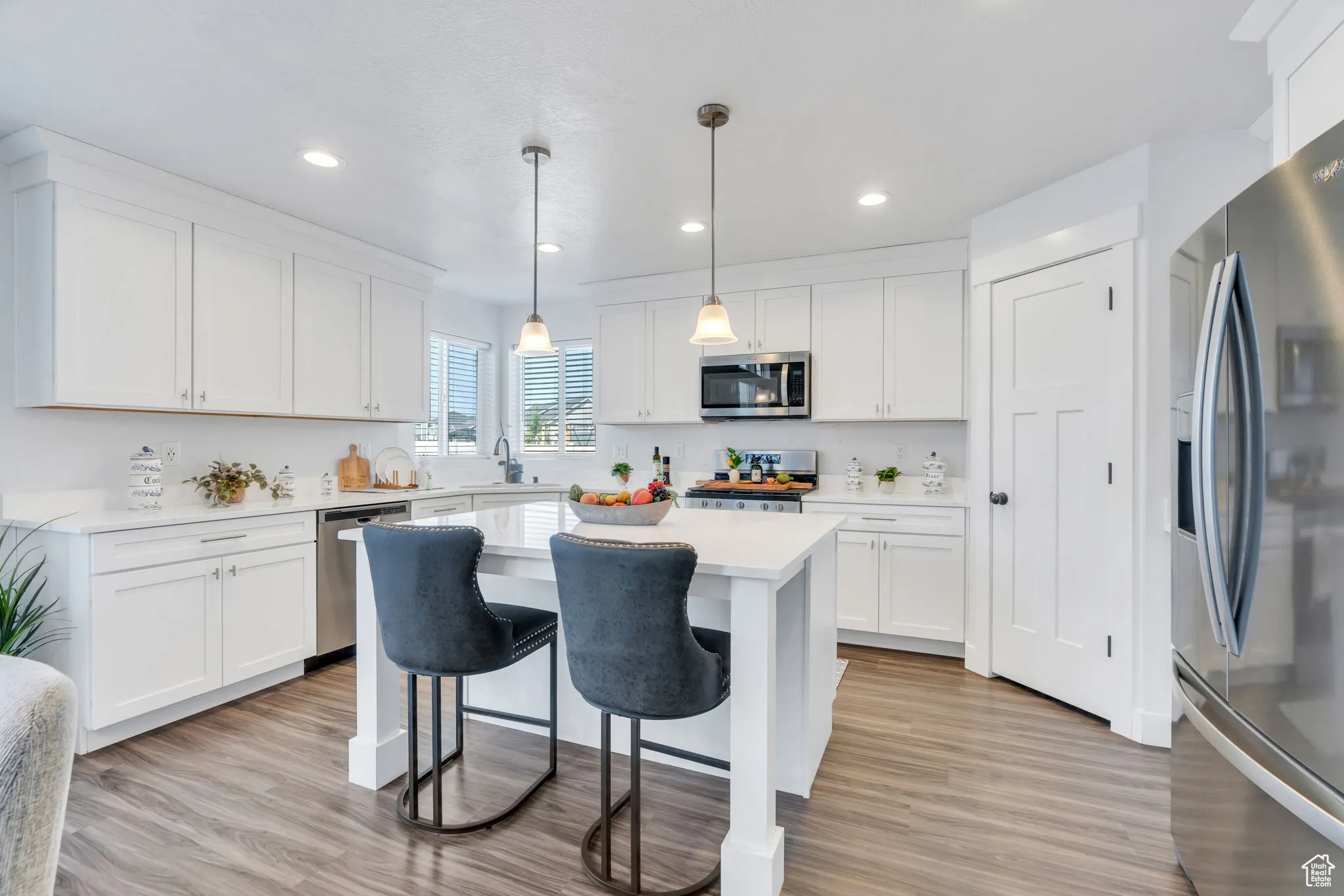 Kitchen with stainless steel appliances, white cabinets, a kitchen bar, light countertops, and recessed lighting