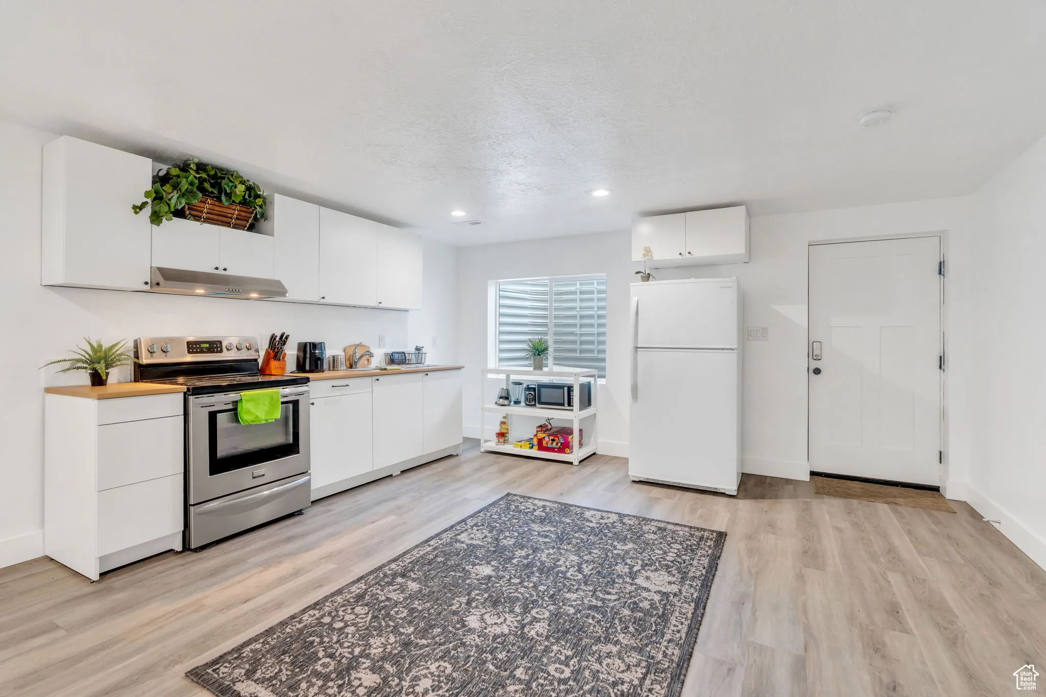 Kitchen featuring stainless steel electric range oven, freestanding refrigerator, light wood-style flooring, white cabinets, and recessed lighting