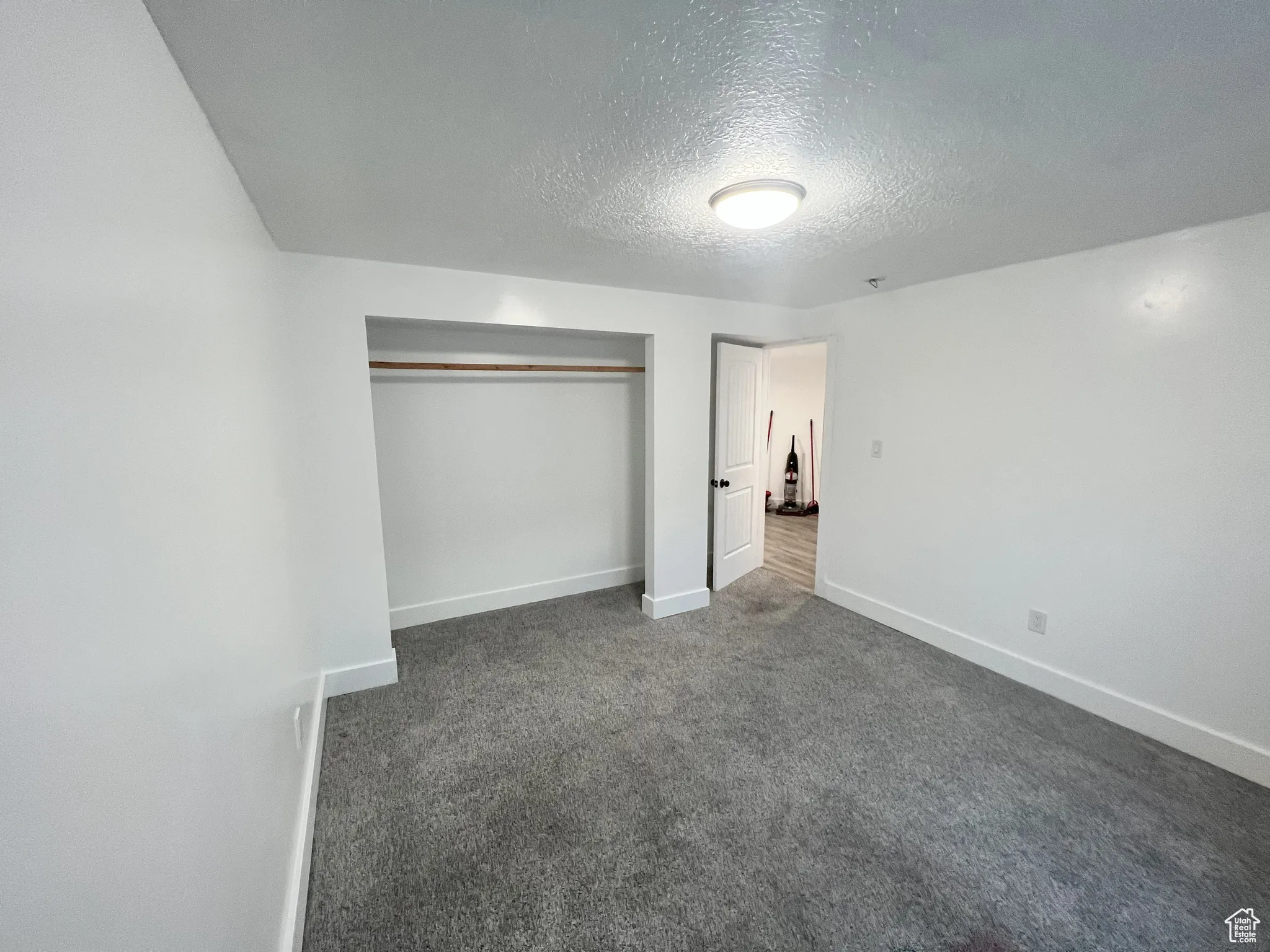 Unfurnished bedroom featuring a textured ceiling, a closet, and dark colored carpet