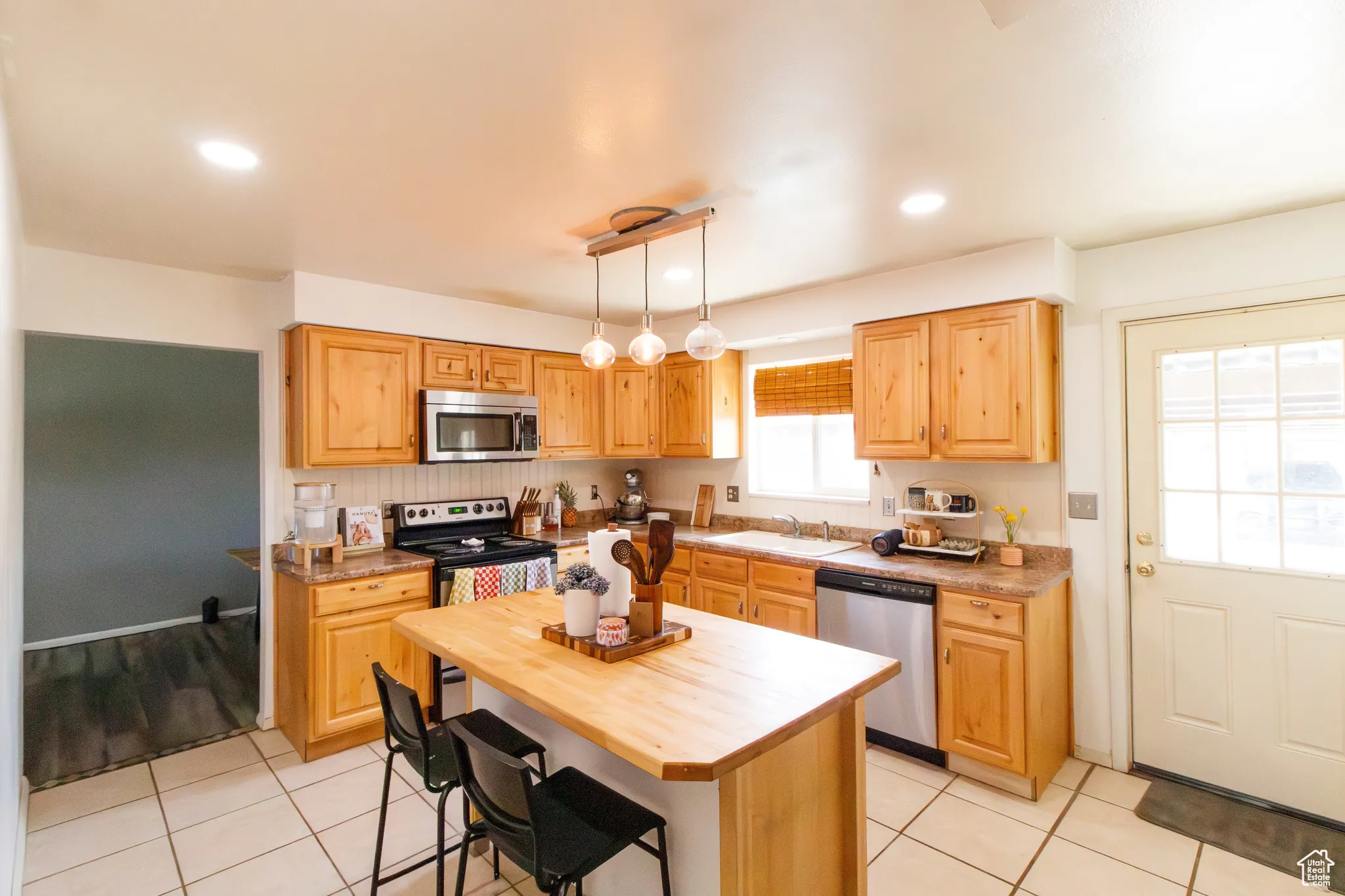 Kitchen featuring wood counters, stainless steel appliances, light tile patterned floors, a kitchen bar, and recessed lighting