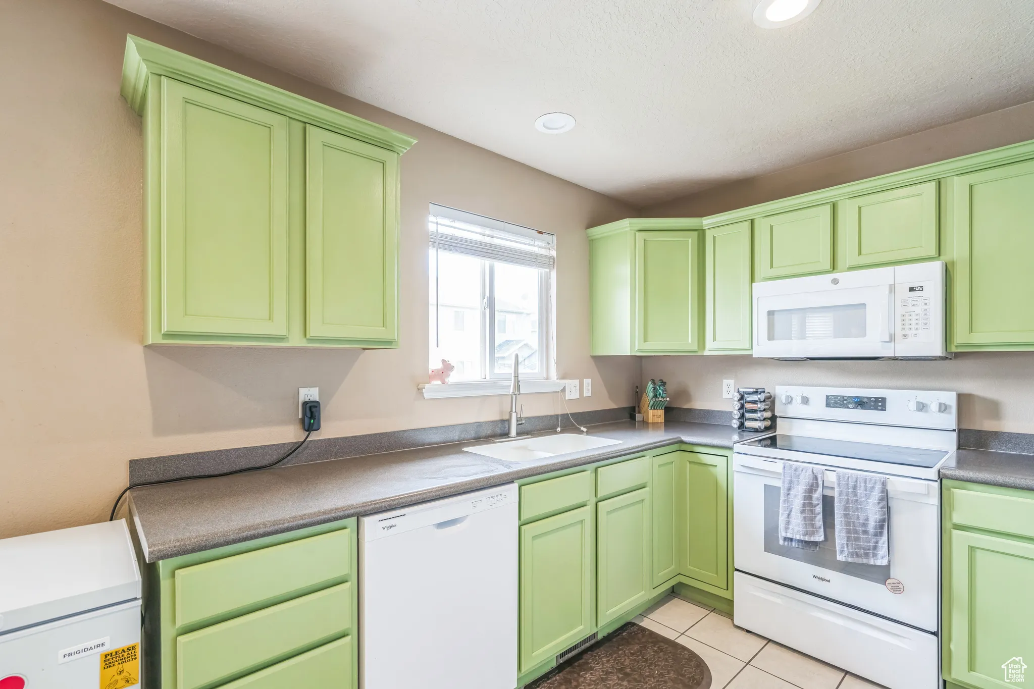 Kitchen featuring white appliances, green cabinetry, light tile patterned flooring, and recessed lighting
